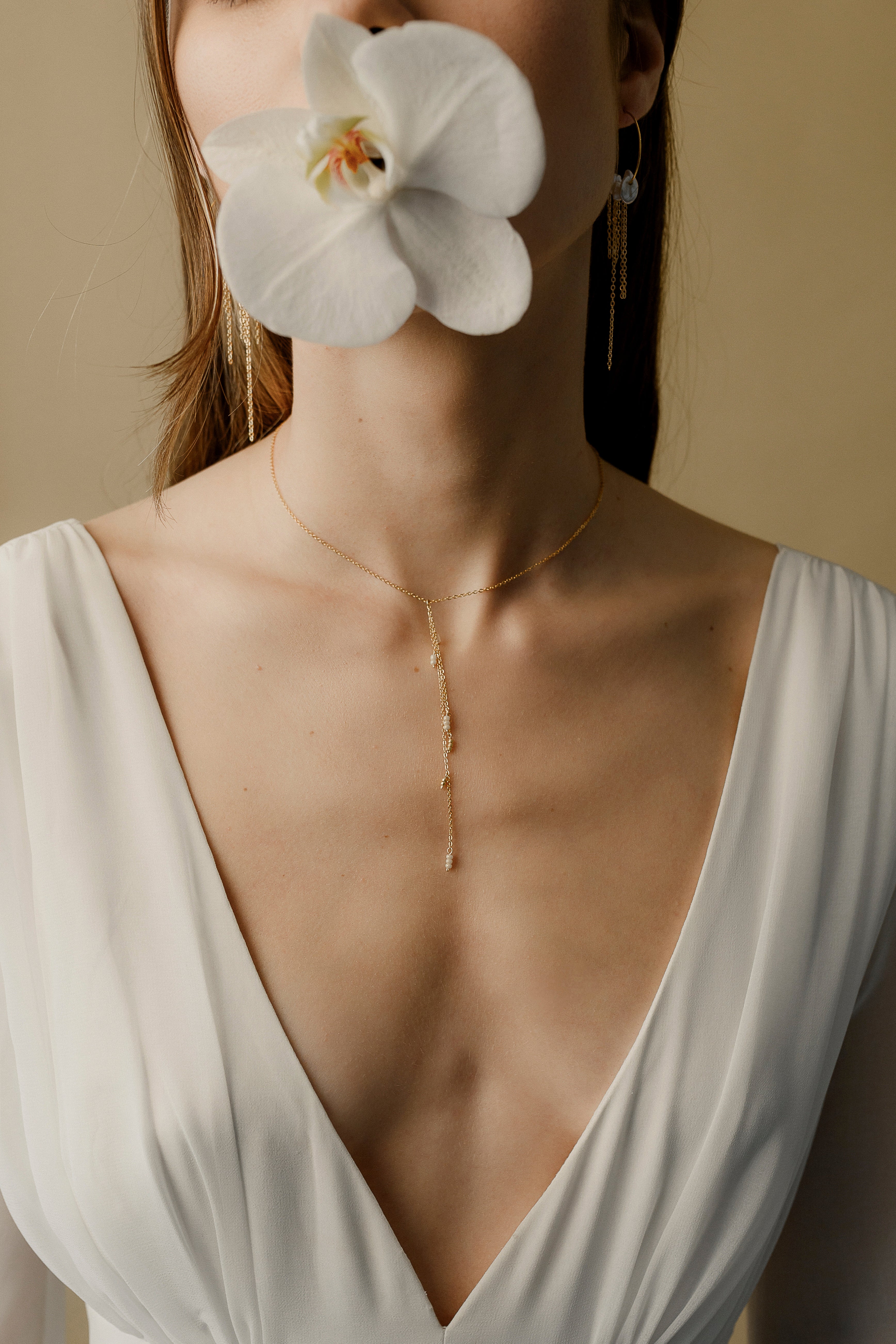 Photo d'une jeune femme avec une orchidée cachant son visage permettant de se focaliser sur son collier de dos qui est également un pendentif sur le devant