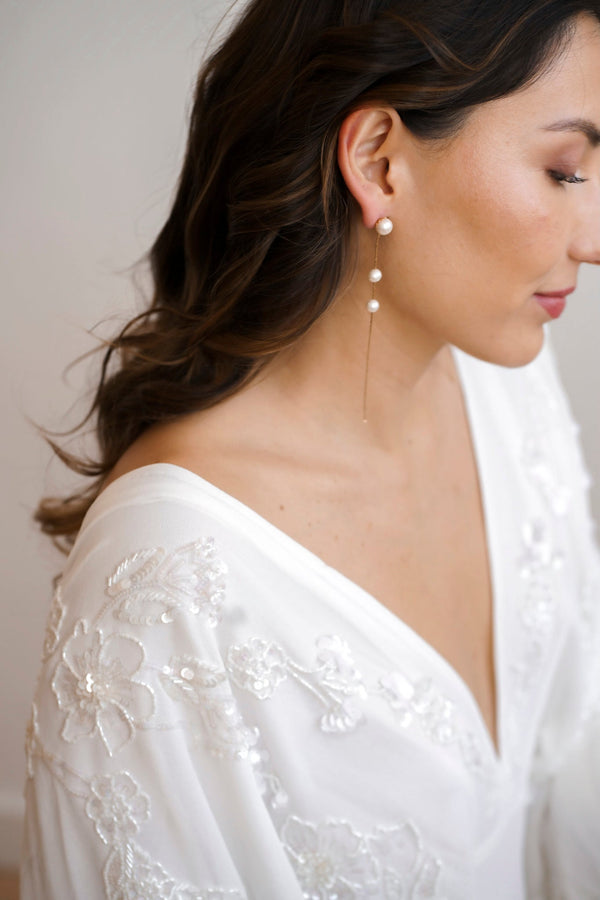 Boucles d'oreilles dorés pendantes avec 3 perles blanches portées par une mariée