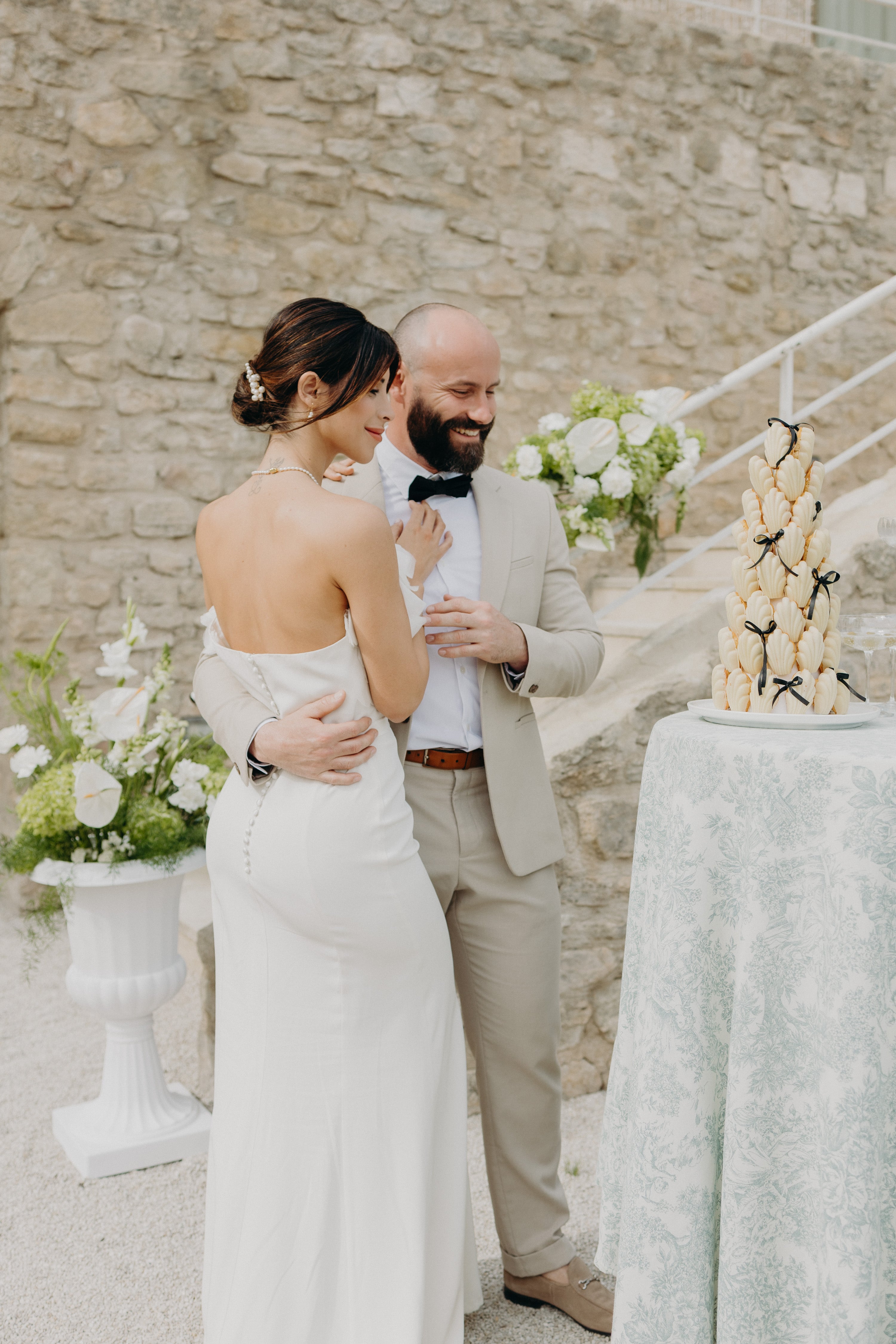 Couple élégant et moderne se tenant devant leur gâteau de mariage pendant leur réception de mariage moderne et naturel sur le thème matcha et olive. Accessoires de mariée subtils et raffinés signés Atelier Lilac.