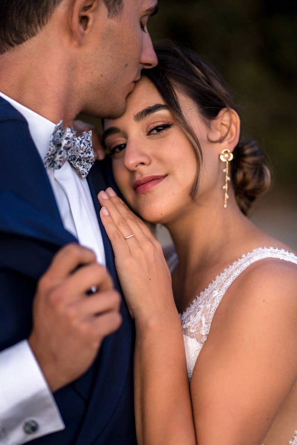 mariée posant sur la photo avec sa main sur le torse de son mari portant des boucles d'oreilles Atelier Lilac en forme de fleurs en or 24k et des cristaux Swarovski 
