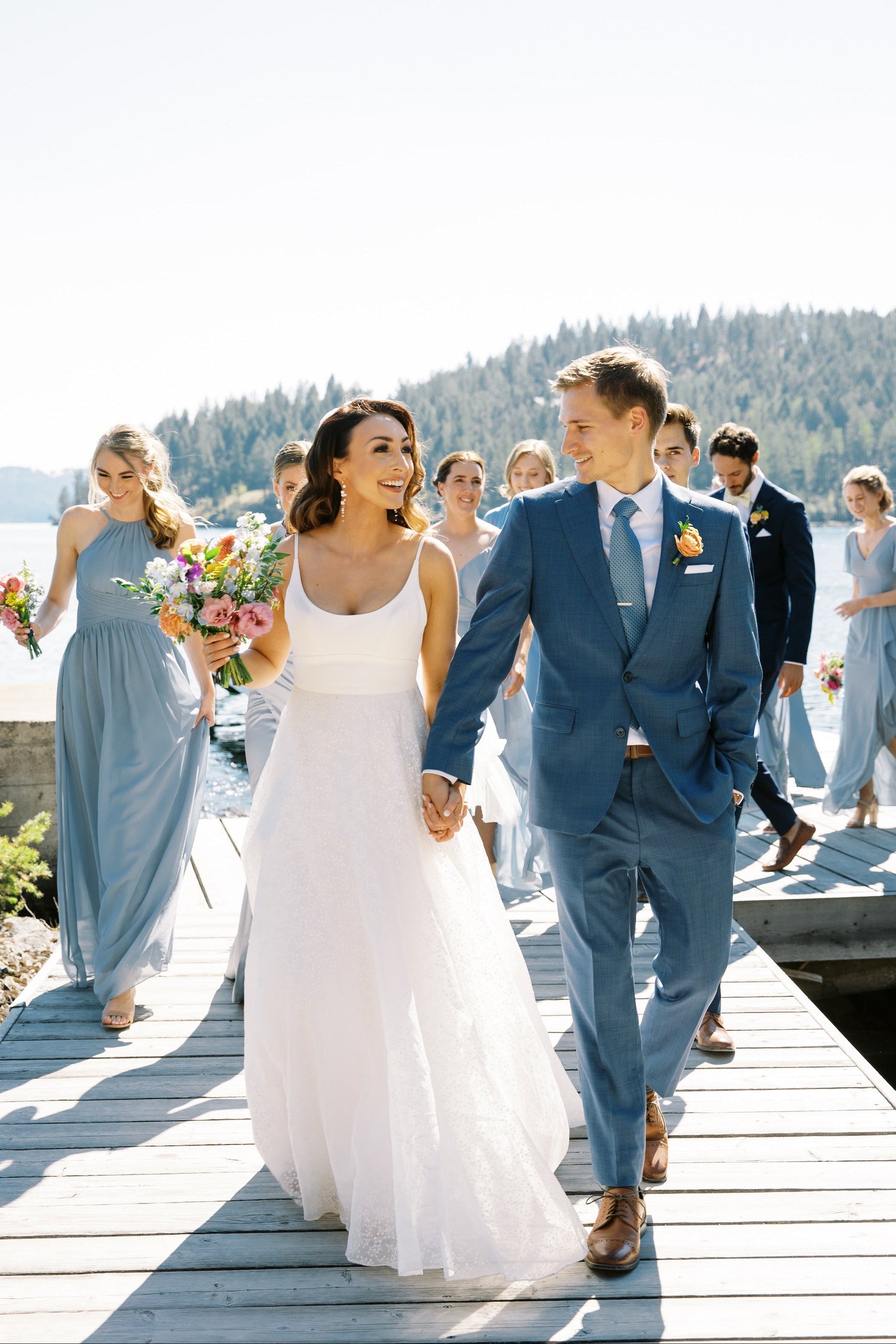 Couple de jeune mariés marchant en souriant avec les demoiselles et garçons d'honneurs qui les suivent