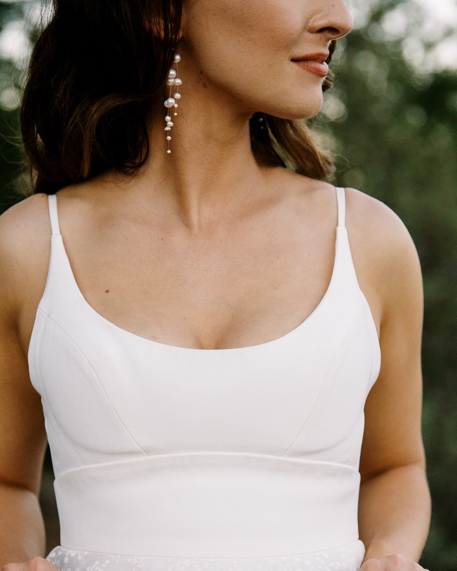 Mariée montrant ses boucles d'oreilles pendante en perles asymétriques sublime avec avec le visage sur le côté 
