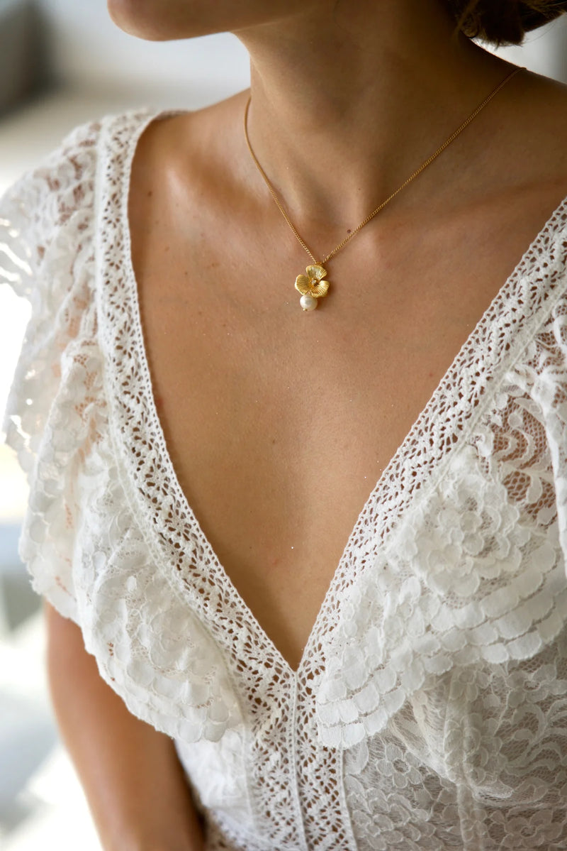 Mariée portant une robe de mariage en dentelle avec un collier en forme de fleurs doré et perle blanche ronde au style bohème et romantique