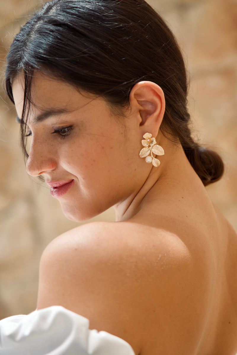 Mariée portant des boucles d'oreilles fleuries en or et perles blanches