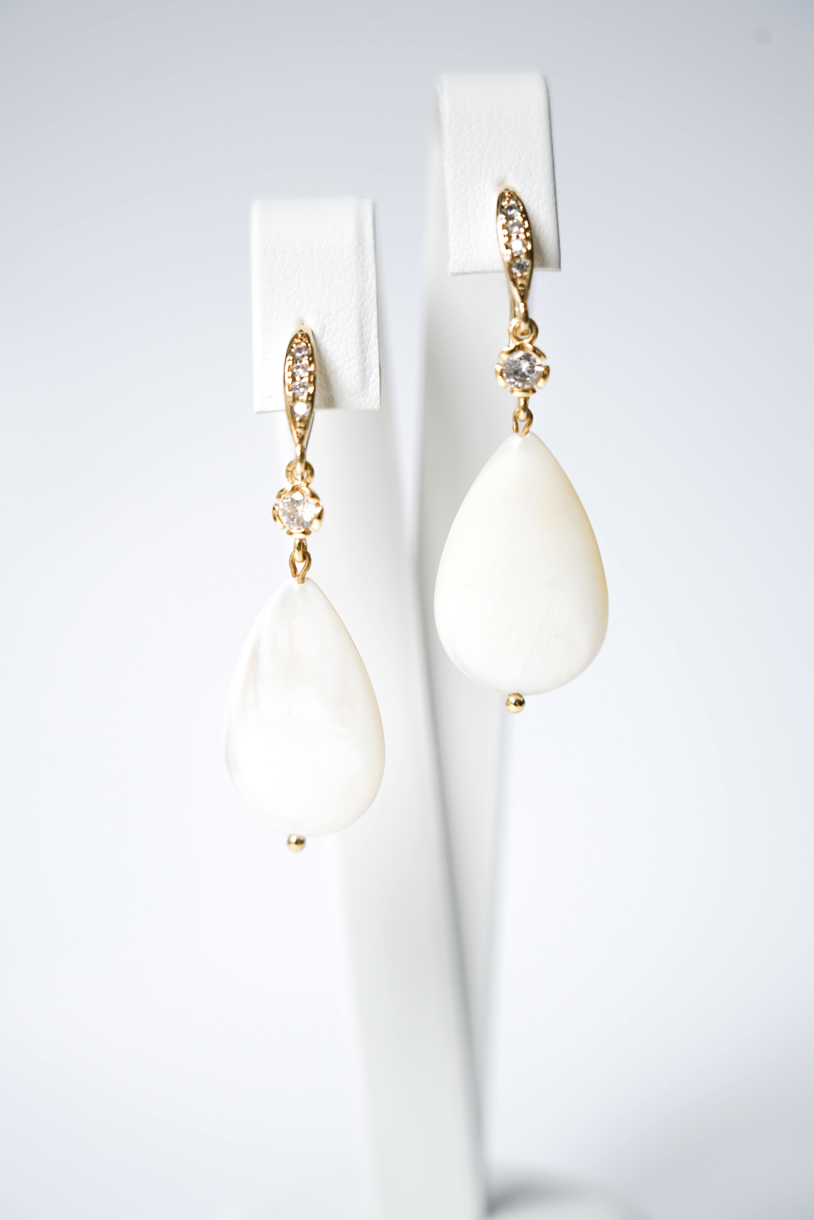 boucles d'oreilles en or avec des petites cristaux et une pièce de nacre blanche sur un fond blanc