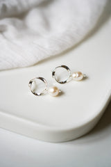 boucles d'oreilles ronde en forme de spirale avec comme pendentif une perle naturelle sur un plateau blanc