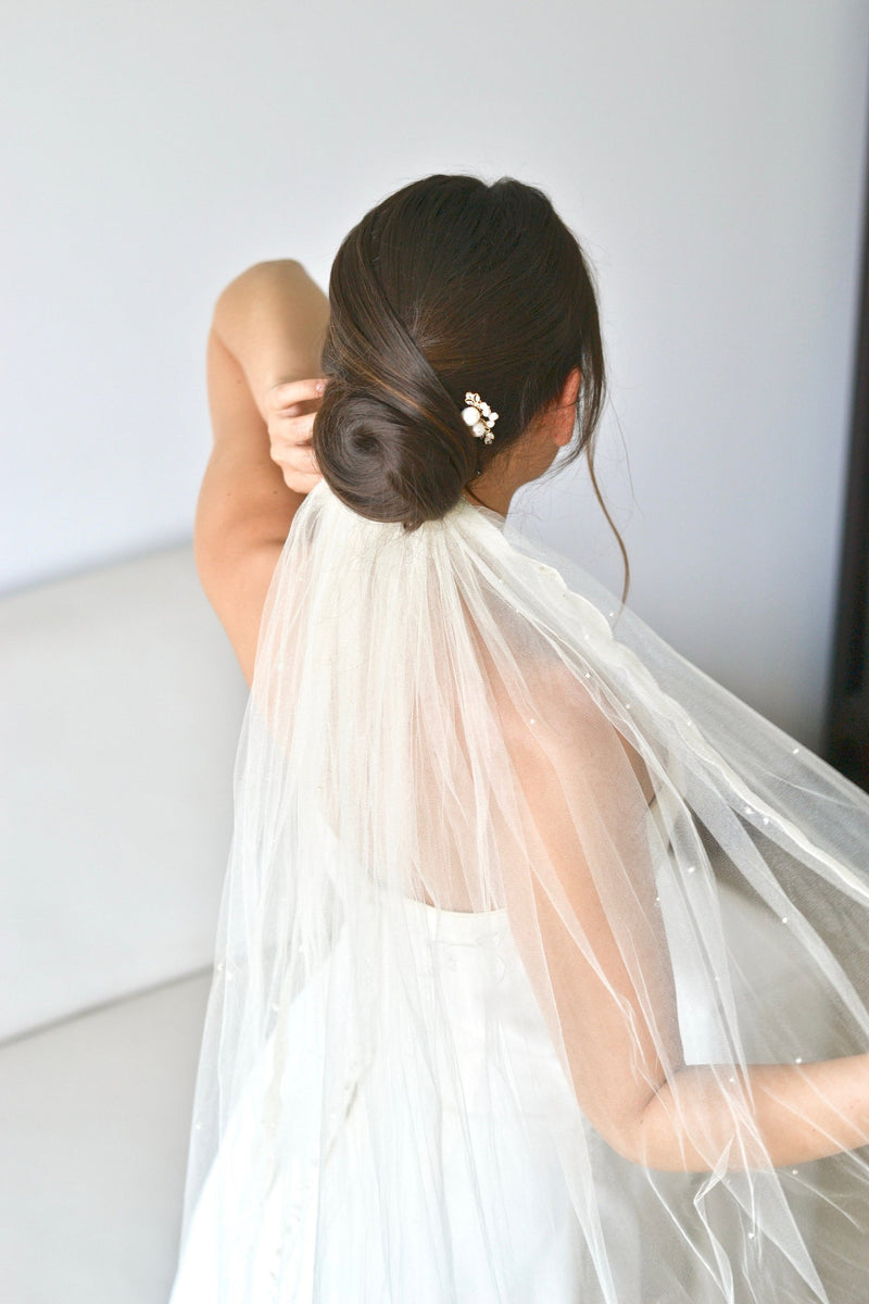 Mariée avec un chignon bas élégant portant un pic à cheveux à perles et cristaux et un voile blanc