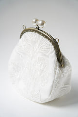 sac de mariage blanc cousu avec un tissu en dentelle fleuri et une attache bronze avec deux perles pour la mariée