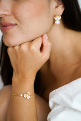 Femme portant un bracelet fait d'une fleur en or et d'une perle naturelle, boucles d'oreilles assorties