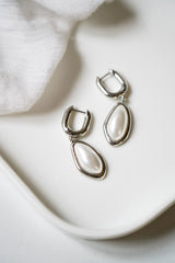 boucles d'oreilles minimaliste avec une perle imparfaite en argent posées sur un fond blanc