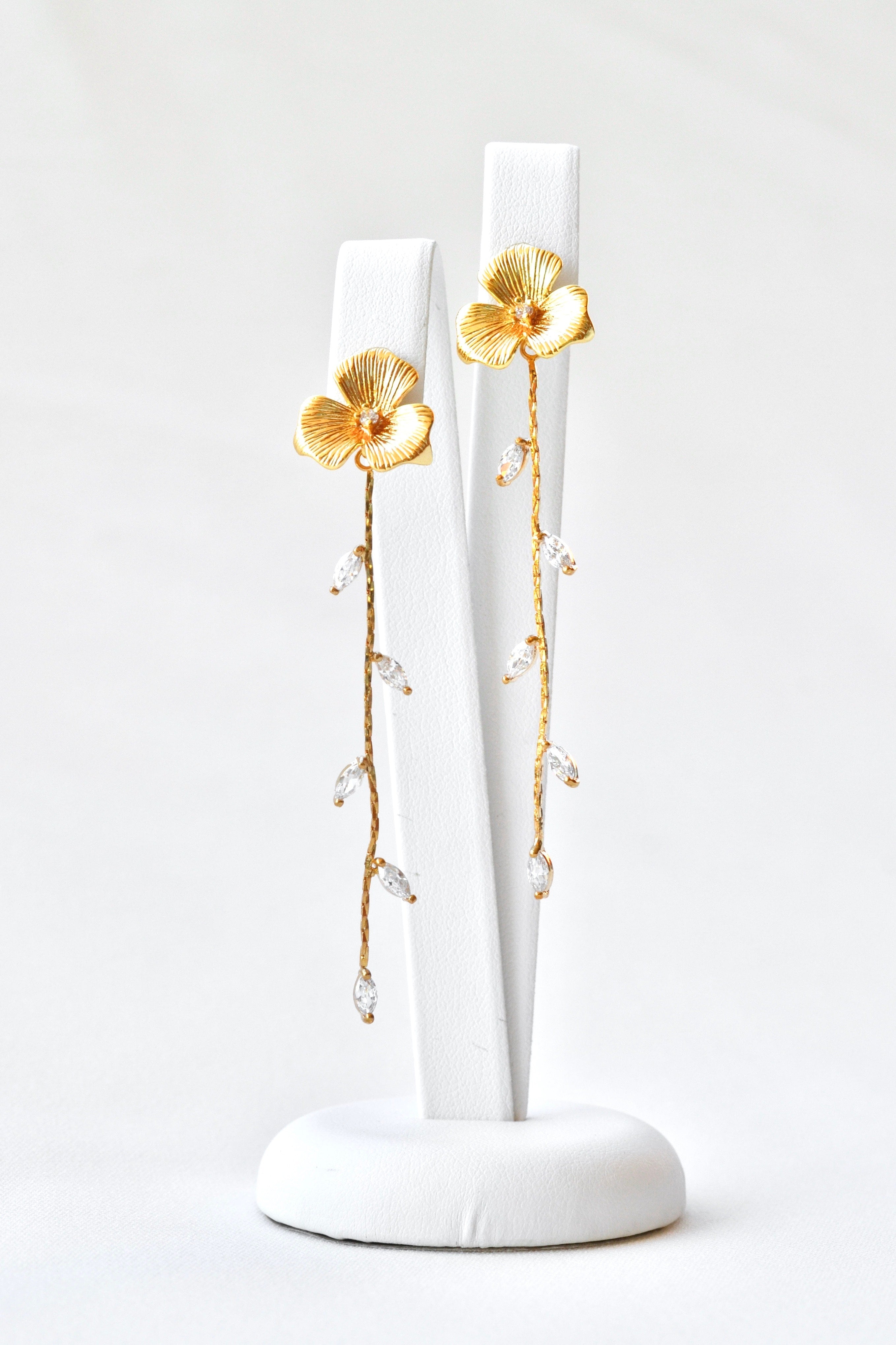 Boucles d'oreilles pendantes fait à la main avec une fleur pour le centre de la boucle et une blanche de feuilles en pendentif sur un socle de bijou blanc