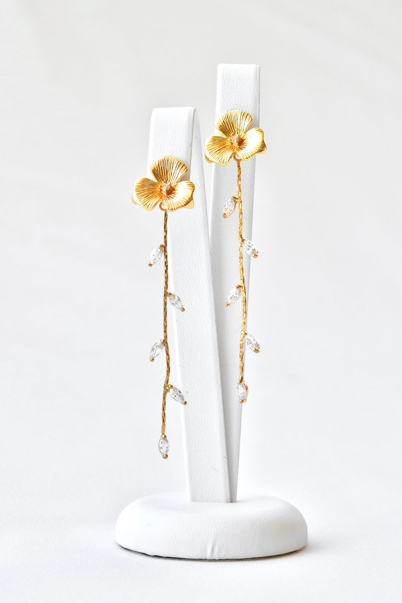 Boucles d'oreilles pendantes fait à la main avec une fleur pour le centre de la boucle et une blanche de feuilles en pendentif sur un socle de bijou blanc