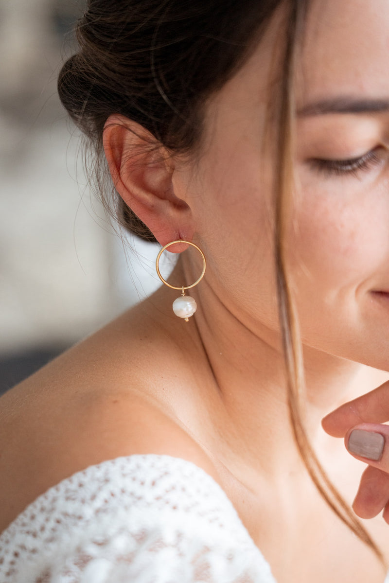 Femme portant des boucles d'oreilles pendantes anneaux dorés et perle blanche