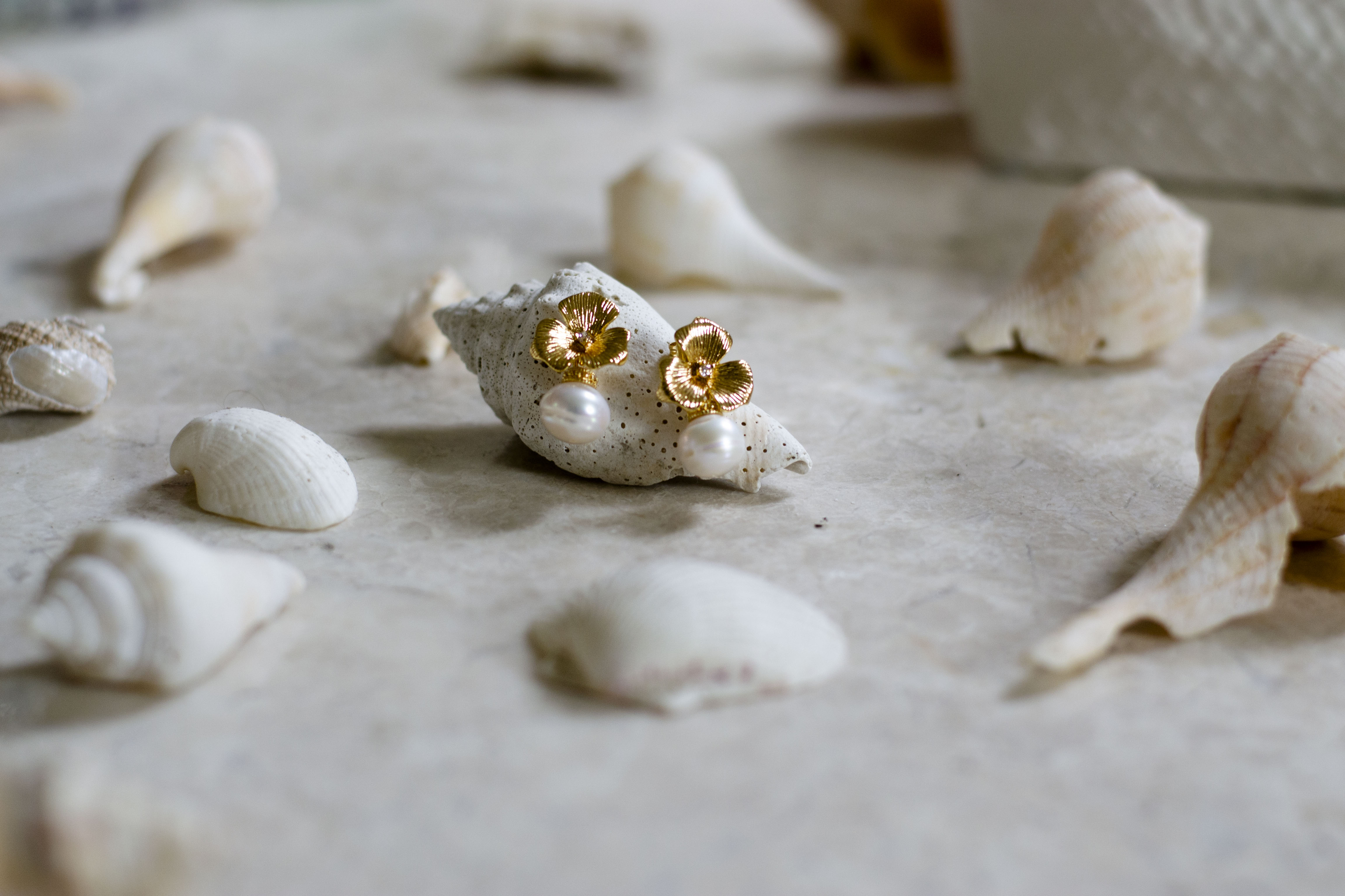 Boucles d'oreilles fleuris or et perles pour un bijoux de mariage romantique sur des coquillages