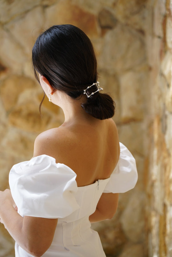 Femme de dos avec une robe blanche épaules dénudées, un chignon élégant avec un élastique à cheveux argent en demi cercle orné de grandes billes argent 