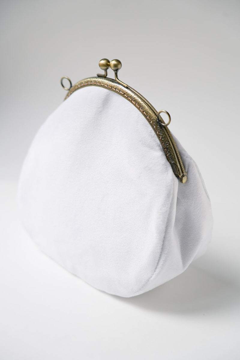 sac pour la mariée le jour de son mariage avec un tissu blanc et une attache vintage en bronze