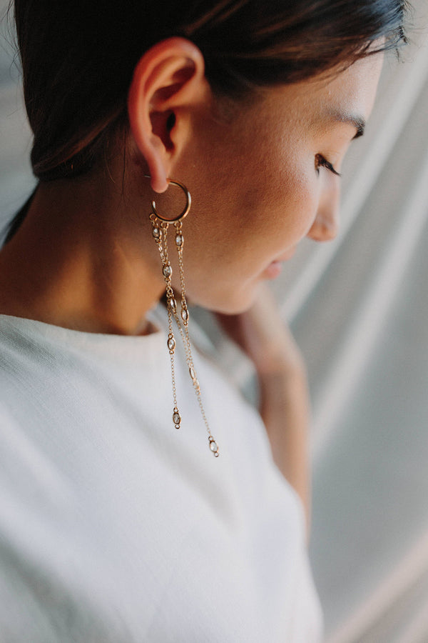 Mariée portant des boucles d'oreilles pendantes bohèmes avec un anneau en or duquel pendent trois chaines ornées de cristaux