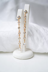 boucles d'oreilles longues pendantes en or et cristaux style vintage et romantique sur un portant à boucles blanc