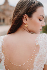 mariée portant des boucles d'oreilles à fleurs dorées, une chaine à cheveux fleurie et un bijou de robe à perles