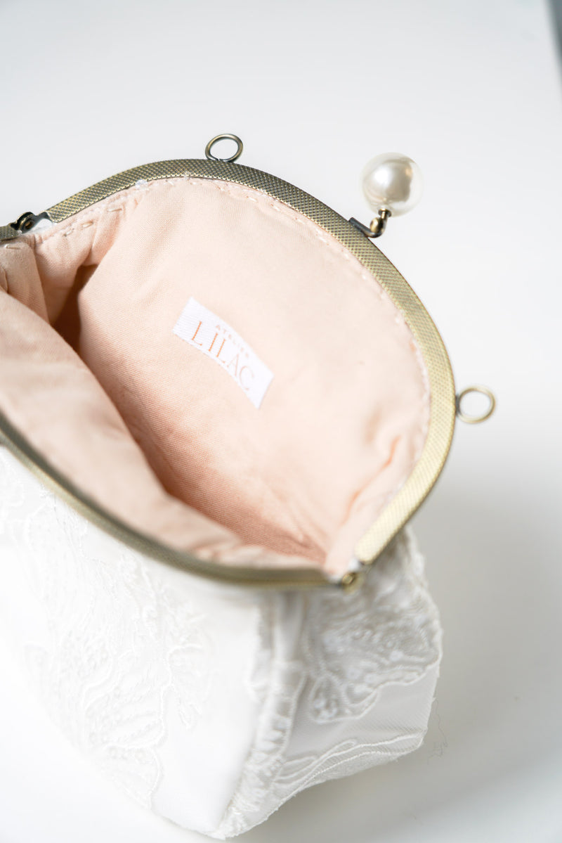 sac de mariage blanc cousu avec un tissu en dentelle fleuri et une attache bronze avec deux perles et l'interieur rose