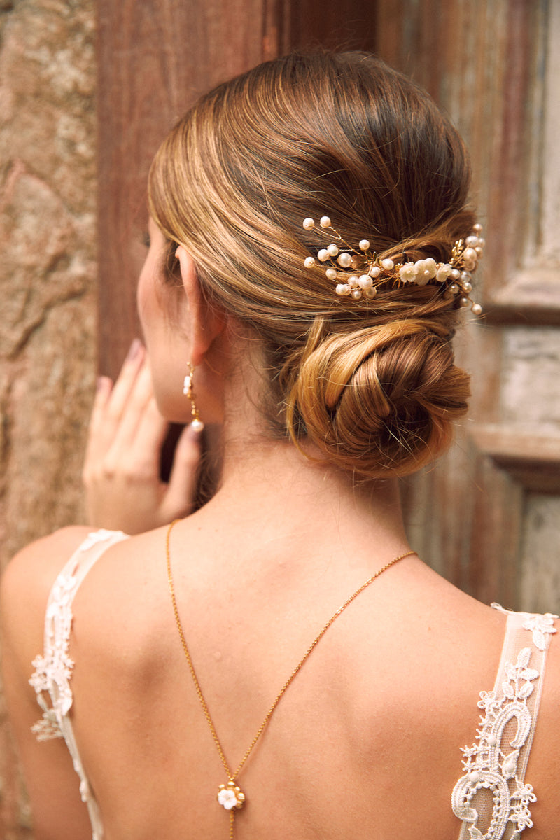 mariée coiffée avec un chignon bas et deux pic de chevaux mariage avec des perles naturelles suivi d'un collier de dos pour son décolleté de robe