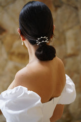 Femme coiffée d'un élégant chignon bas de mariée avec un élastique à cheveux avec un structure en demi-cercle argent moderne et minimaliste