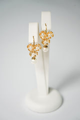 Boucles d'oreilles trois fleurs dorées ornées de perles sur un support