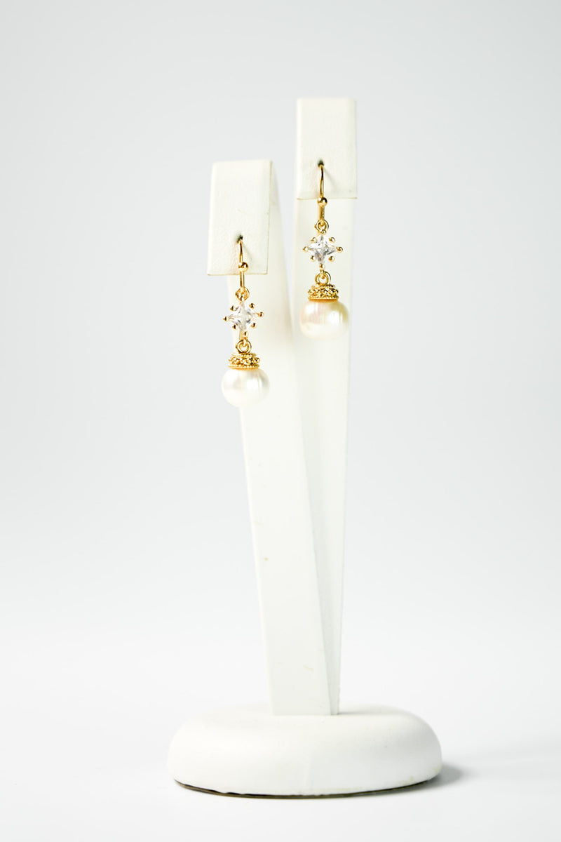 boucles d'oreilles pour mariage avec un cristaux et une perle en pendentif sur un socle de bijou vu de loin