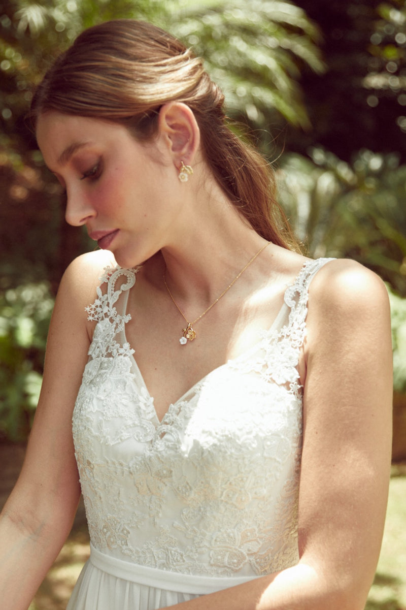 Mariée portant un collier romantique à fleurs or et blanches et des boucles d'oreilles de mariage romantique assorties