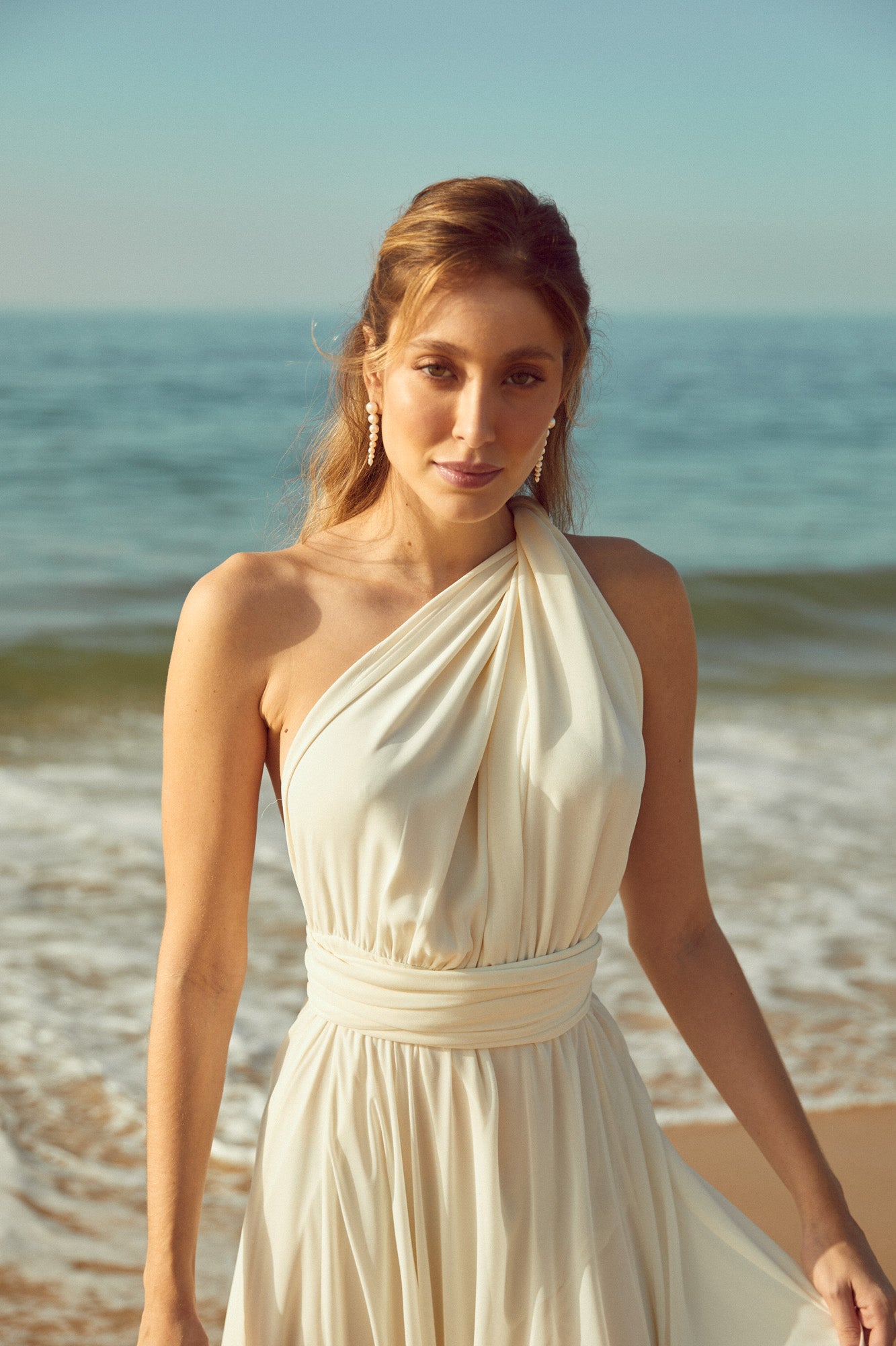 mariée sur la plage qui porte des boucles d'oreilles en perles et une robe blanche souriante