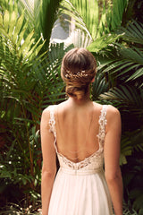 Mariée portant un pic à cheveux de mariage à perles sur un chignon bohème, des boucles d'oreilles pendantes à perles et un collier de dos à double chaînes devant un décor tropical 