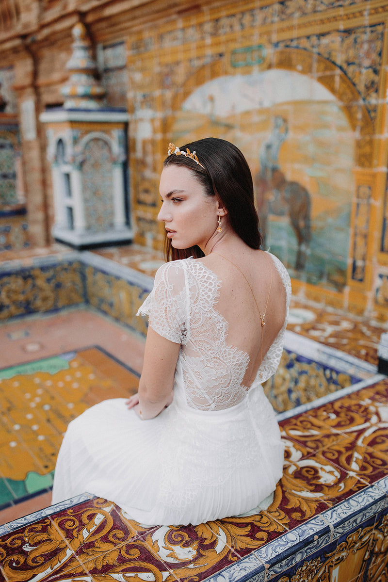 mariée sur un banc en mosaïque à Séville portant un collier de dos floral et un couronne bohème