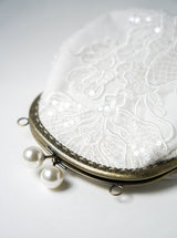 sac de mariage blanc cousu avec un tissu en dentelle fleuri et une attache bronze avec deux perles prise de près