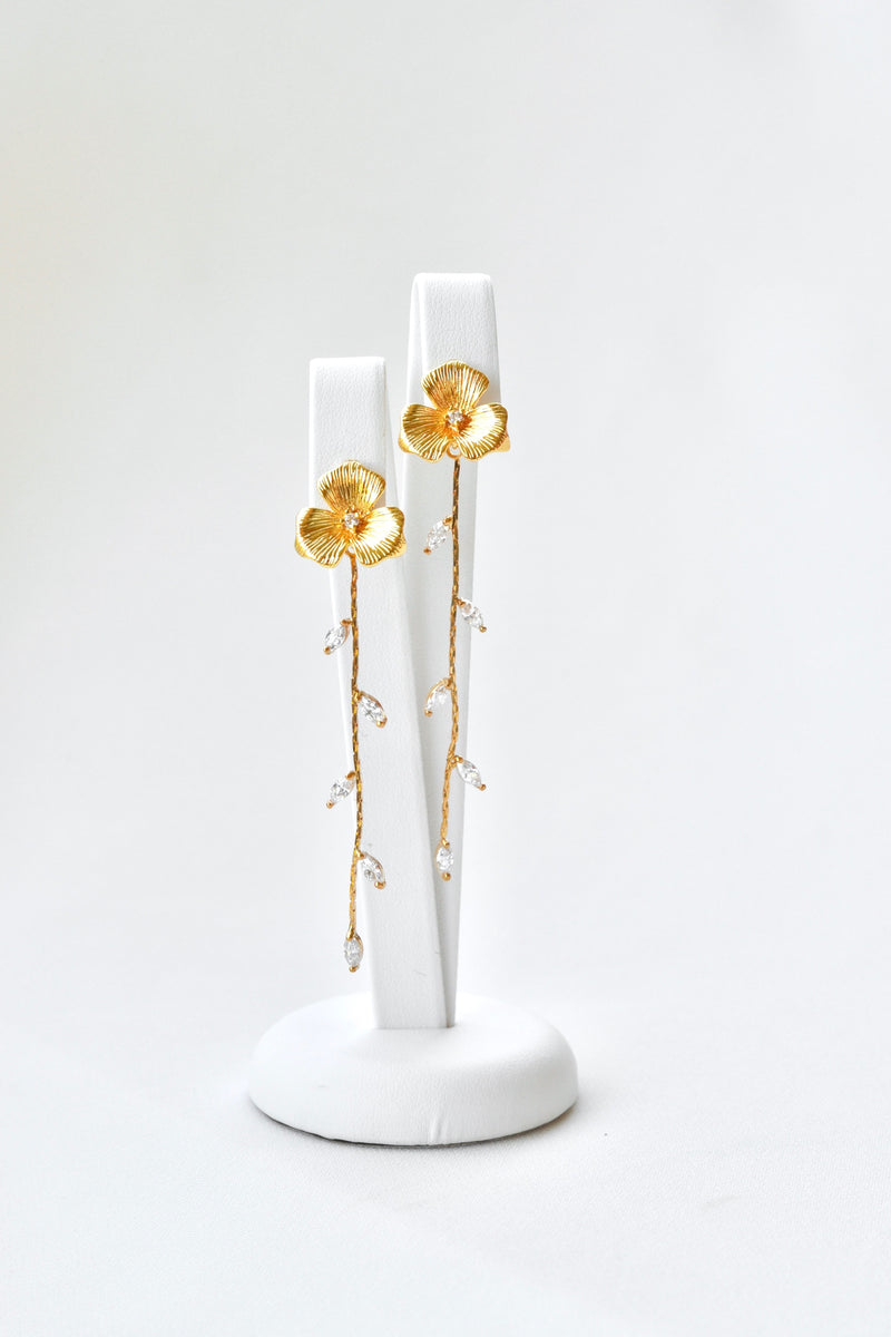 Boucles d'oreilles pendantes fait à la main avec une fleur pour le centre de la boucle et une blanche de feuilles en pendentif sur un fond blanc