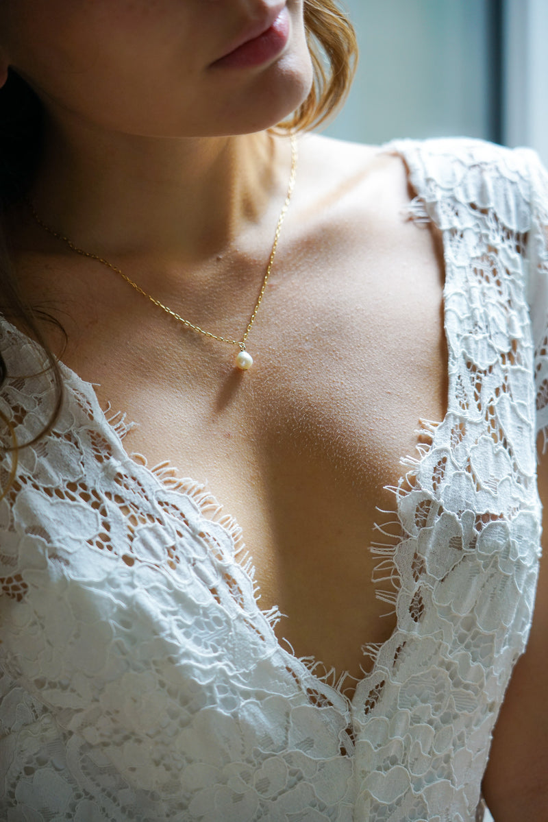 collier en or ave une perle en pendentif sur une mariée en robe blanche à dentelle