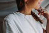Mariée portant des boucles d'oreilles pendantes bohèmes et romantiques avec un anneau en or duquel pendent trois chaines ornées de cristaux