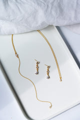 collier de dos et boucles d'oreilles en or et cristaux style vintage bohème posé sur un plateau blanc