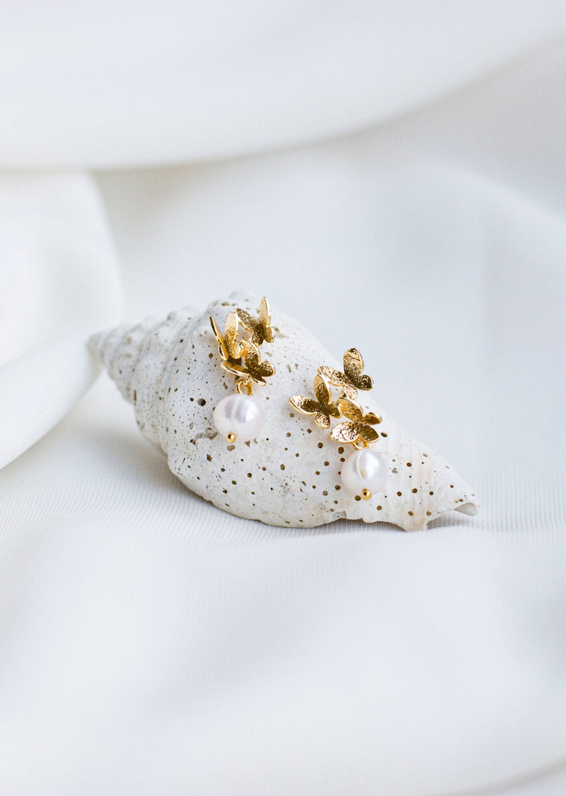 Boucles d'oreilles mariage papillons dorées et perles naturelles sur un coquillage