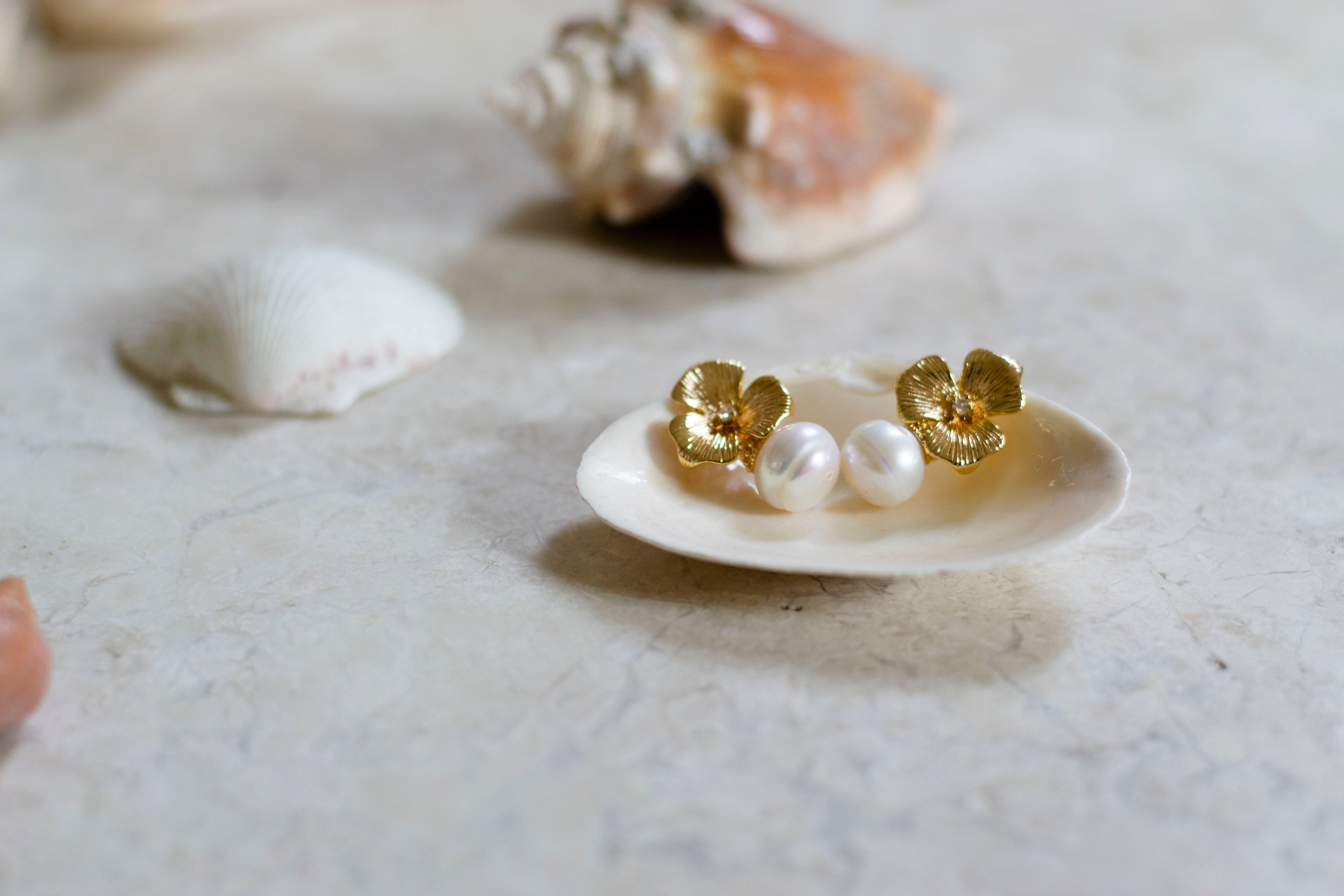 Boucles d'oreilles mariage à fleur en or et perle posées sur un coquillage