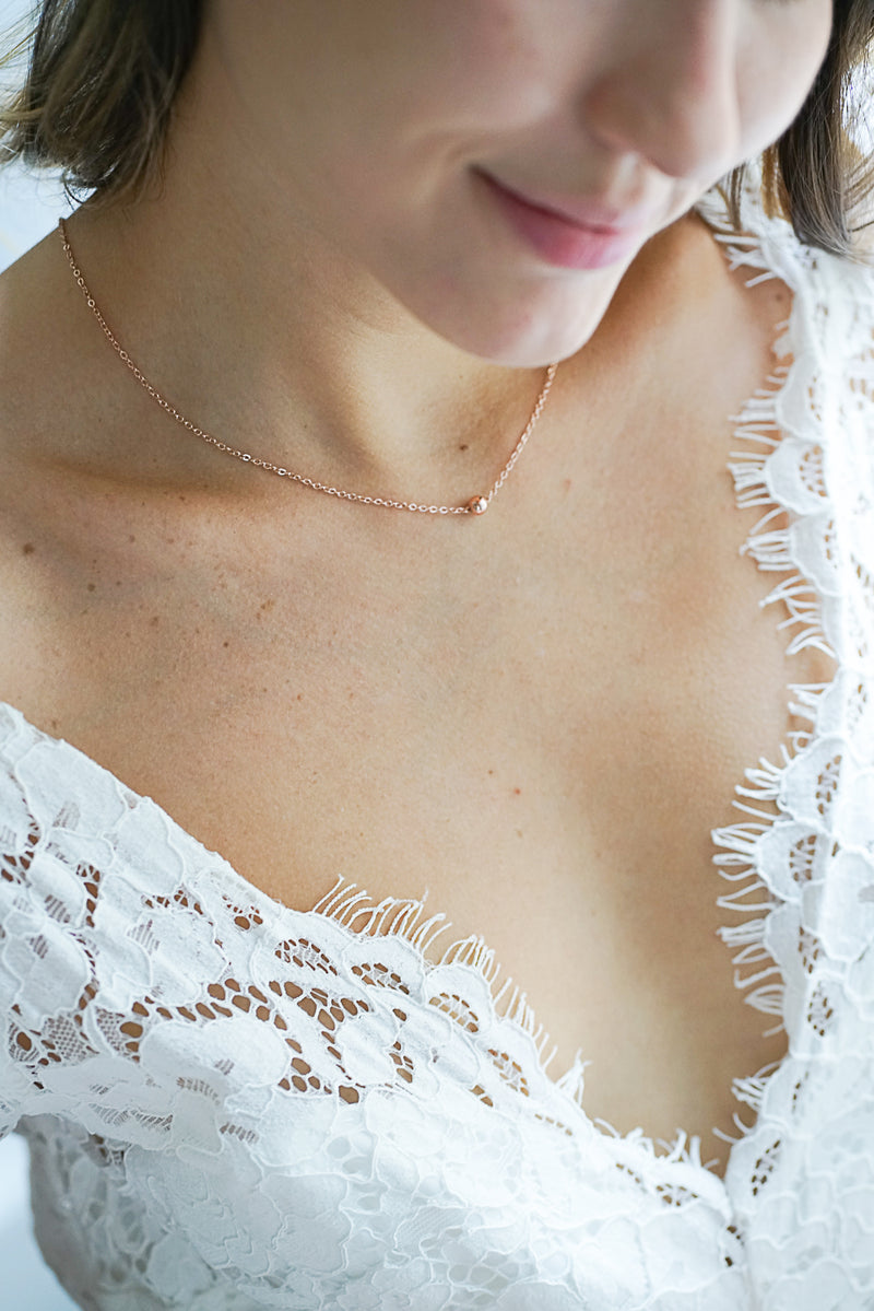mariée portant un collier avec un pendentif bille en or rose et une robe en dentelle prise en photo de près