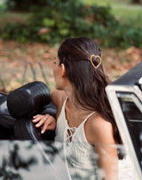 Femme dans une voiture décapotable avec une barrette en forme de coeur torsadé or