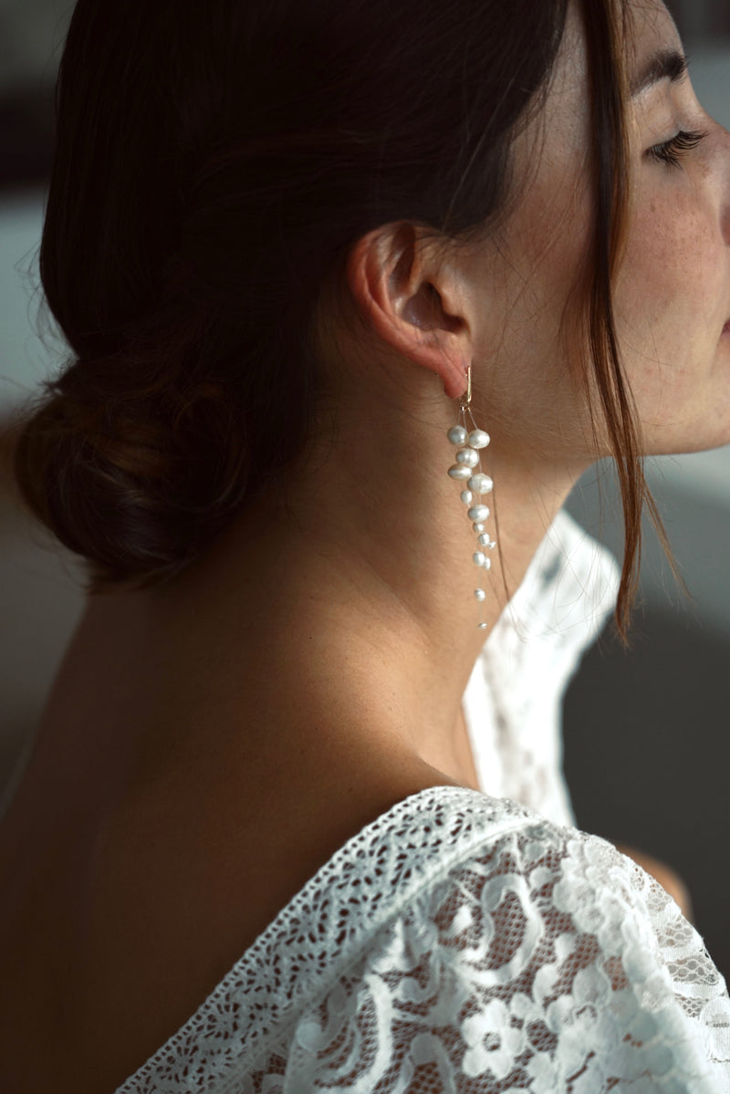 Mariée portant des boucles d'oreilles pendantes raffinées fait de trois fils transparents auxquels sont enfilées de belles perles naturelles blanches