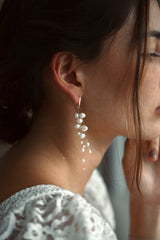 Mariée portant des boucles d'oreilles pendantes bohèmes et élégantes fait de trois fils transparents auxquels sont enfilées de belles perles naturelles blanches