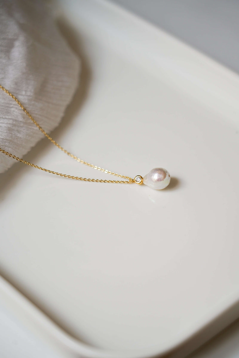 Collier long en or avec une perle minimaliste sur un plateau blanc