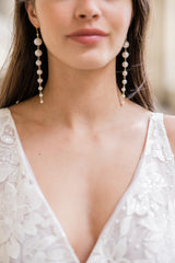 Mariée portant des boucles d'oreilles pendantes à 8 perles naturelles au style minimaliste et élégant