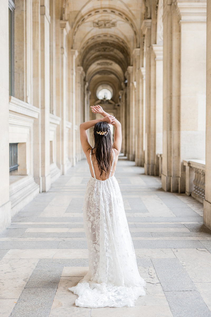 Mariée sous des arches parisiens avec un longue robe de mariée bohème et un peigne bohème à fleurs et perles