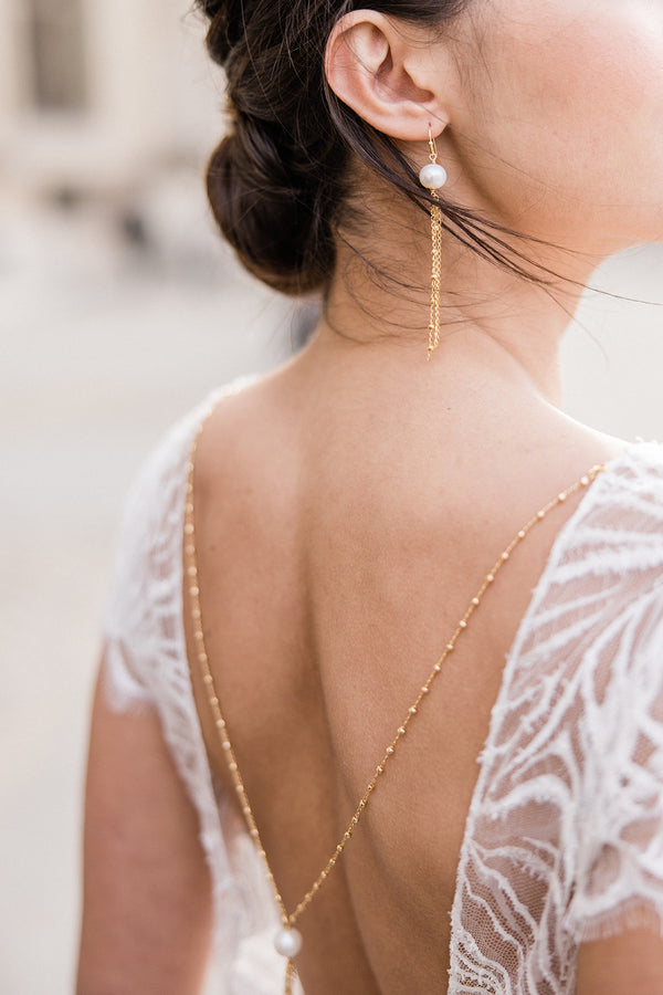 Mariée portant des boucles d'oreilles pendantes à perles naturelles et chaines dorées et collier de dos assorti 