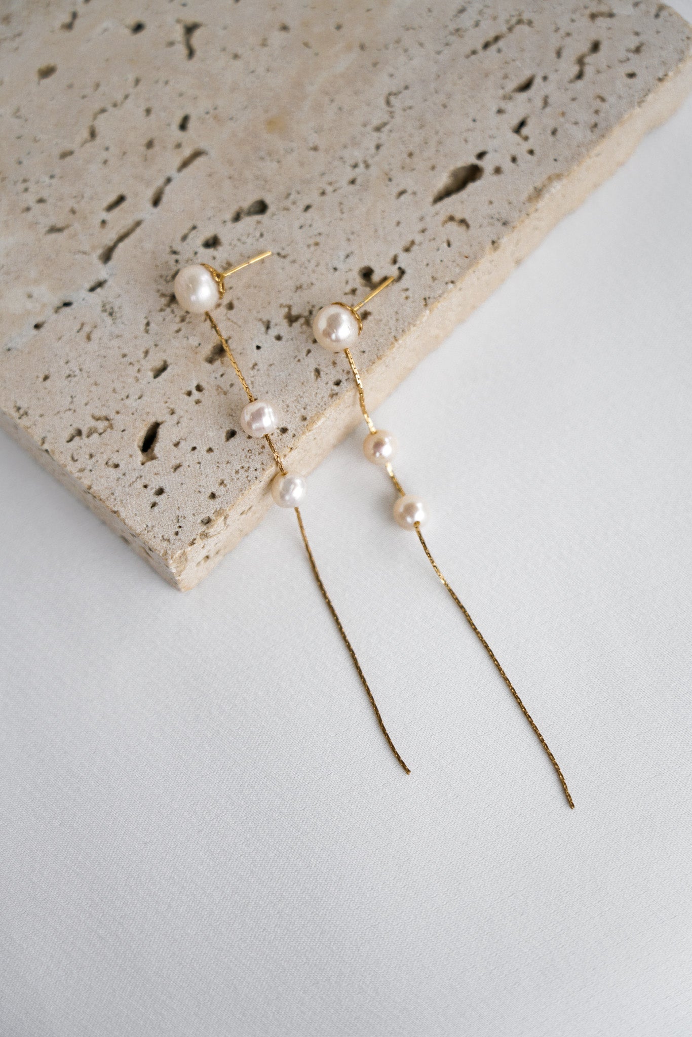 Boucles d'oreilles pendantes faites de trois perles naturelles accrochées à une chaine dorée
