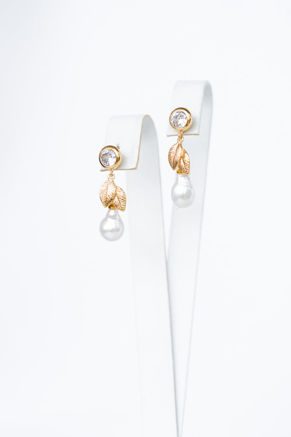 boucles d'oreilles bohème avec un zircon, un feuille en or et une perle naturelle sur un socle de bijoux blanc