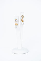 boucles d'oreilles bohème avec un zircon, un feuille en or et une perle naturelle de face sur un socle à bijoux blanc